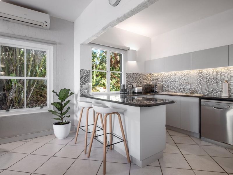 Modern kitchen featuring granite countertops, mosaic tile backsplash, sleek cabinetry, and a breakfast bar, complemented by natural light and split-system air conditioning.
