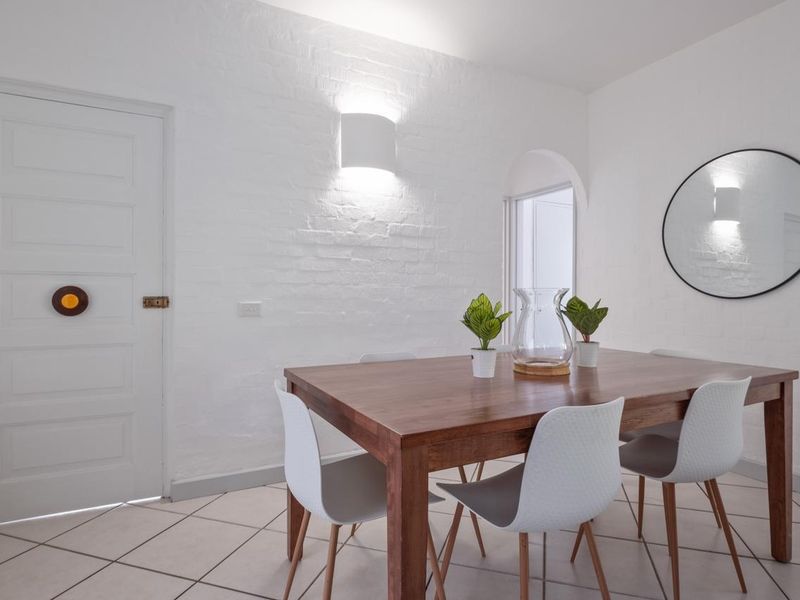 A bright dining room featuring white painted brick walls, tiled flooring, and an arched doorway leading to an adjacent space.