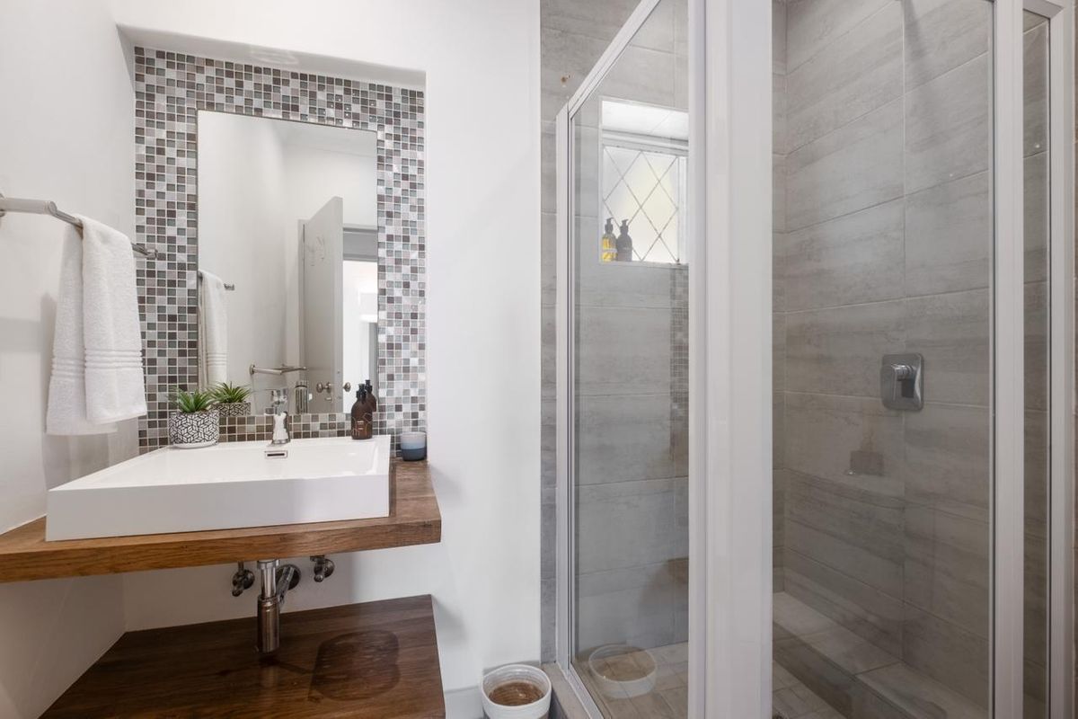 Modern bathroom featuring a vessel sink on a wooden vanity, mosaic tile accents, and a glass-enclosed shower with neutral wall tiling.