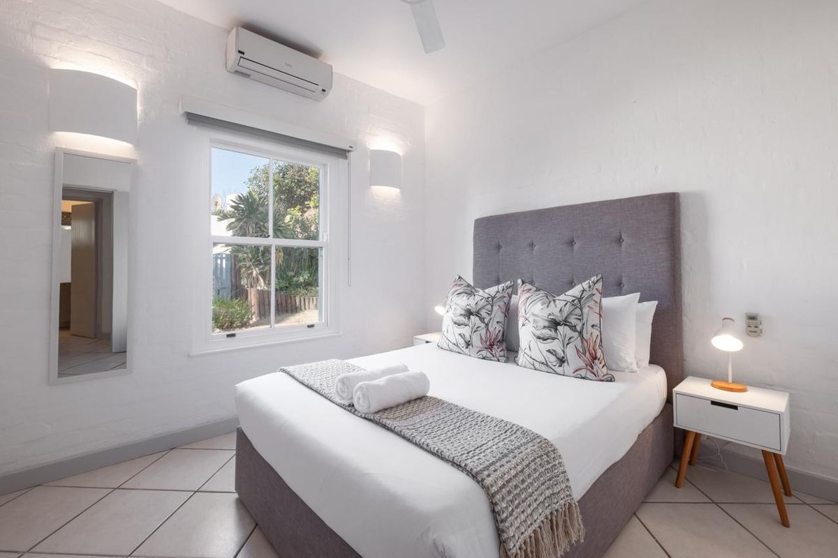A bright and well-maintained bedroom featuring tiled flooring, a split-system air conditioner, ceiling fan, and a sash window overlooking the garden.