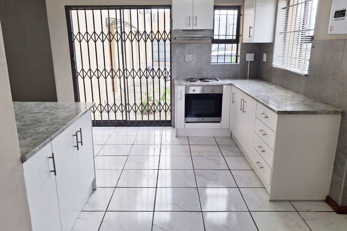 A clean, modern kitchen featuring white cabinetry, stone-look laminate countertops, built-in oven and hob, and tiled flooring with direct access to the exterior.