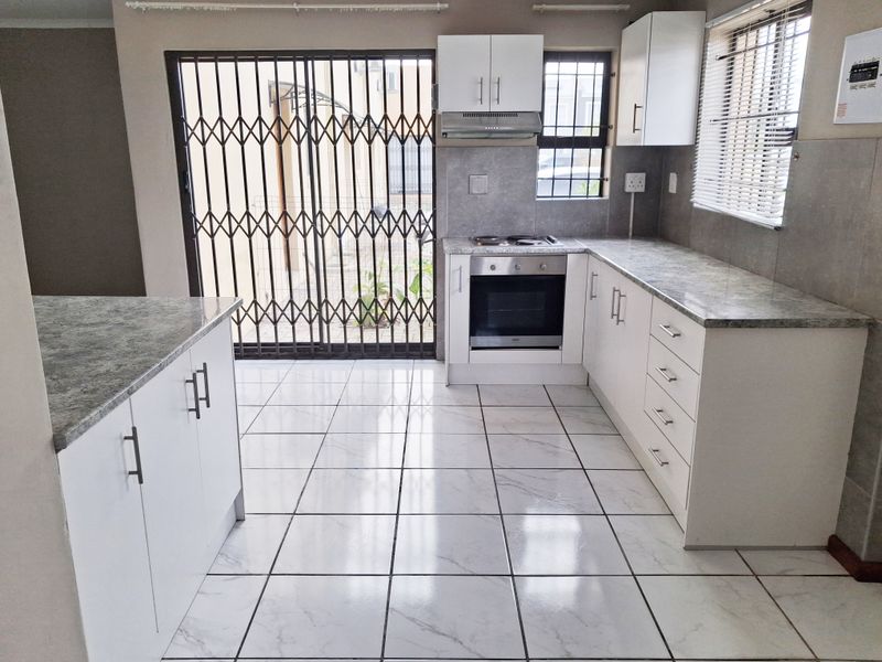 A clean, modern kitchen featuring white cabinetry, stone-look laminate countertops, built-in oven and hob, and tiled flooring with direct access to the exterior.