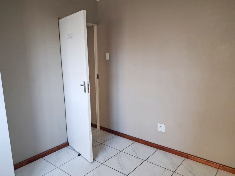 An empty bedroom featuring neutral wall paint, white tiled flooring, and wooden skirting boards, providing a clean canvas for personalization.