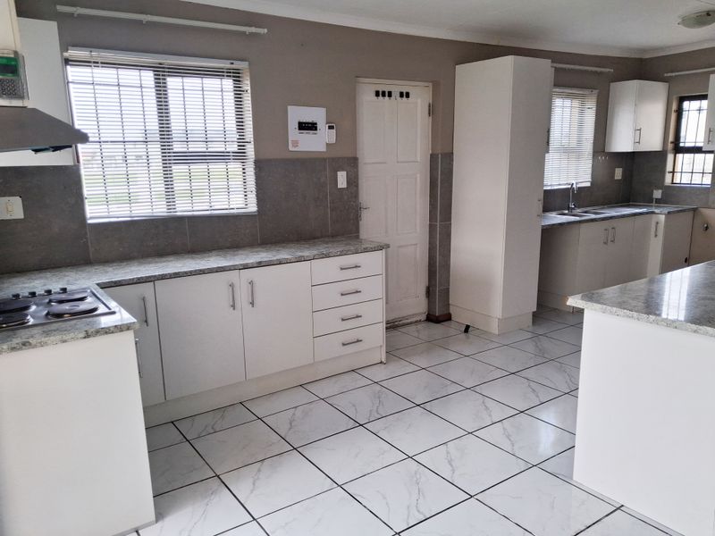 A clean, functional kitchen featuring white cabinetry, granite countertops, tiled flooring, and integrated appliances, offering a bright and well-maintained workspace.