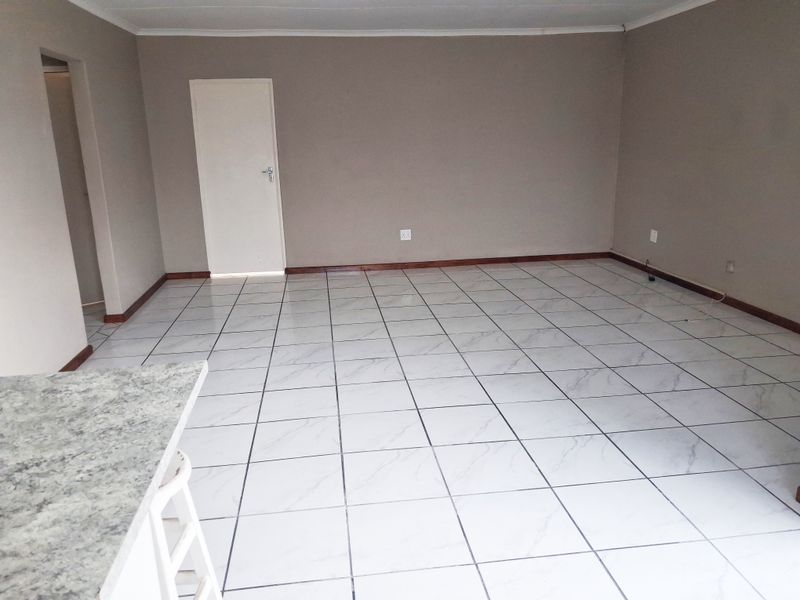 A spacious, empty open-plan living area featuring neutral wall tones and clean, light-colored tiled flooring throughout.