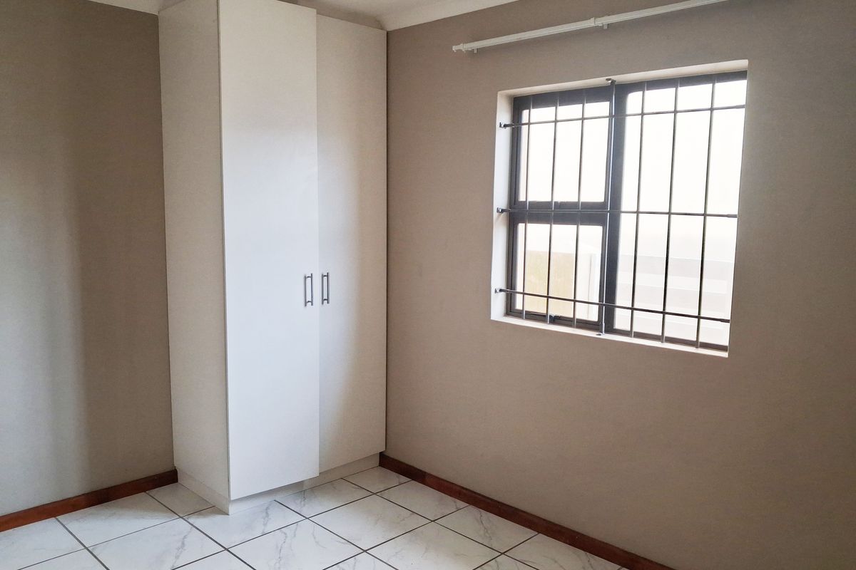 A clean, empty bedroom featuring neutral wall paint, white tiled flooring, and a built-in wardrobe with security bars on the window.