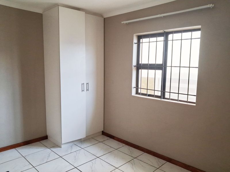 A clean, empty bedroom featuring neutral wall paint, white tiled flooring, and a built-in wardrobe with security bars on the window.