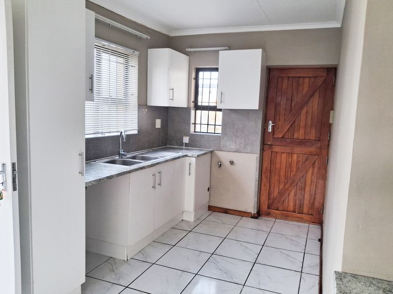 A functional kitchen featuring white cabinetry, laminate countertops, a double basin sink, and tiled flooring, with direct access via a timber stable door.