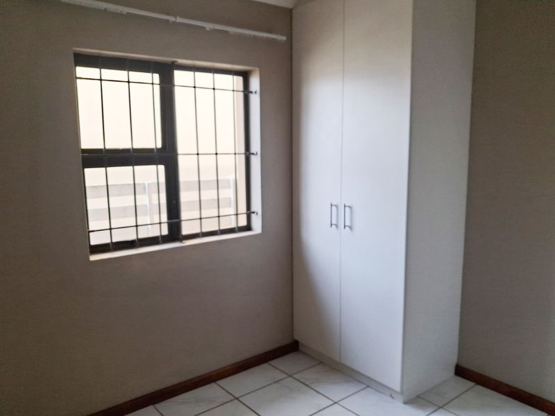 A clean, empty bedroom featuring tiled flooring, a built-in wardrobe, and a window fitted with security bars.
