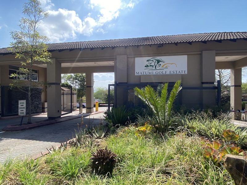 The main entrance gatehouse of Matumi Golf Estate, featuring a paved driveway, professional signage, and well-maintained landscaped garden areas.