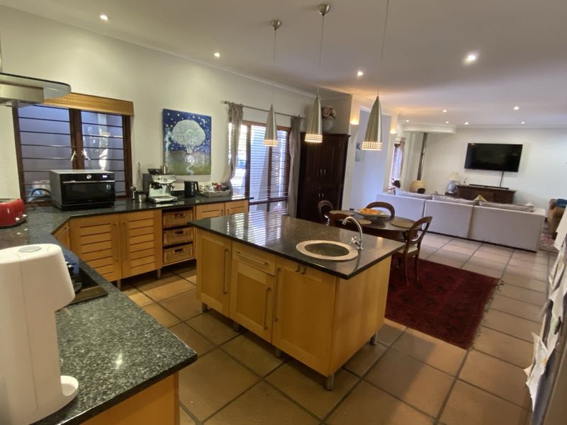 Spacious open-plan kitchen and living area featuring a central island, granite countertops, warm timber cabinetry, and tiled flooring throughout.