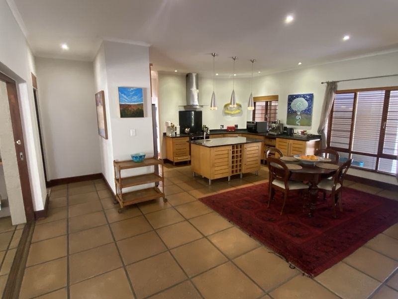 Spacious open-plan kitchen and dining area featuring wooden cabinetry, a central island, tiled flooring, and ample natural light through large windows.