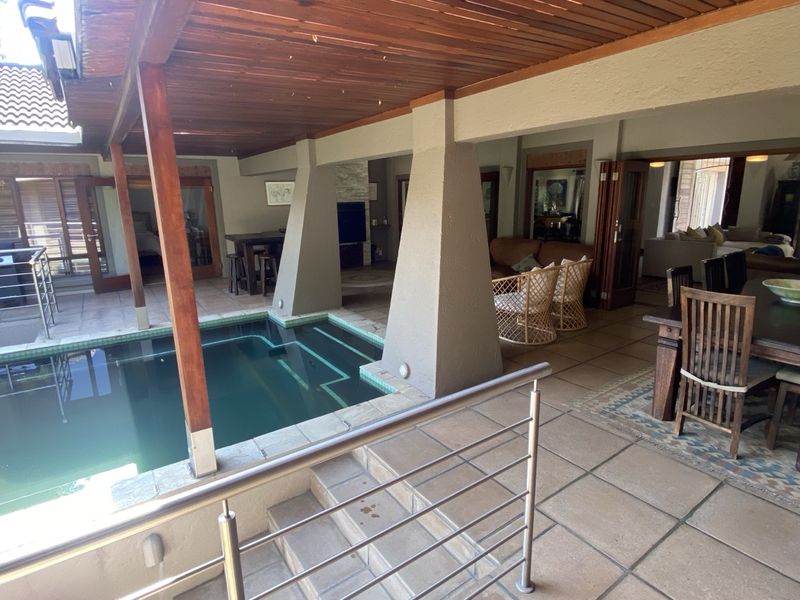 Covered patio area featuring a built-in swimming pool, timber ceiling, and tiled flooring, providing seamless indoor-outdoor flow through large stacking doors.