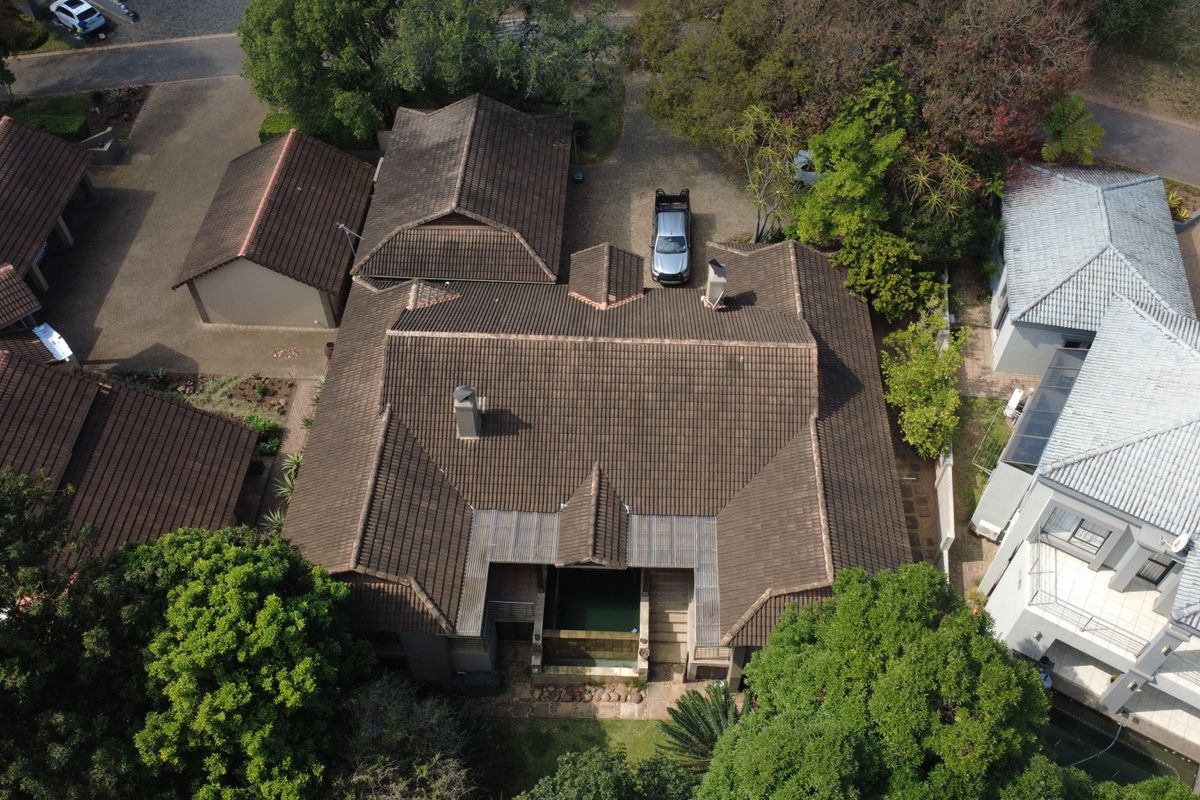 Aerial view of the property showcasing the tiled roof structure, chimneys, swimming pool area, and surrounding driveway and garden space.