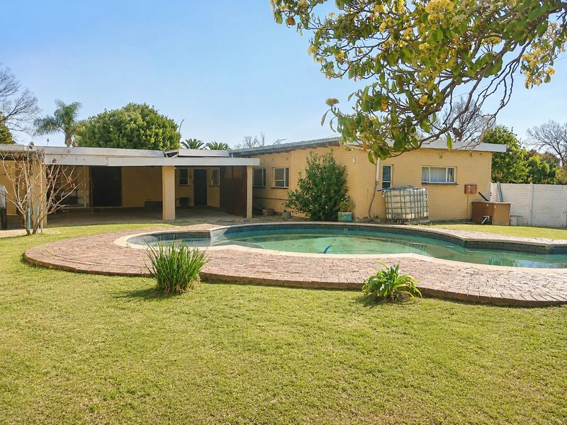 Rear exterior view featuring a swimming pool with brick paving, a covered patio area, and a spacious lawn.