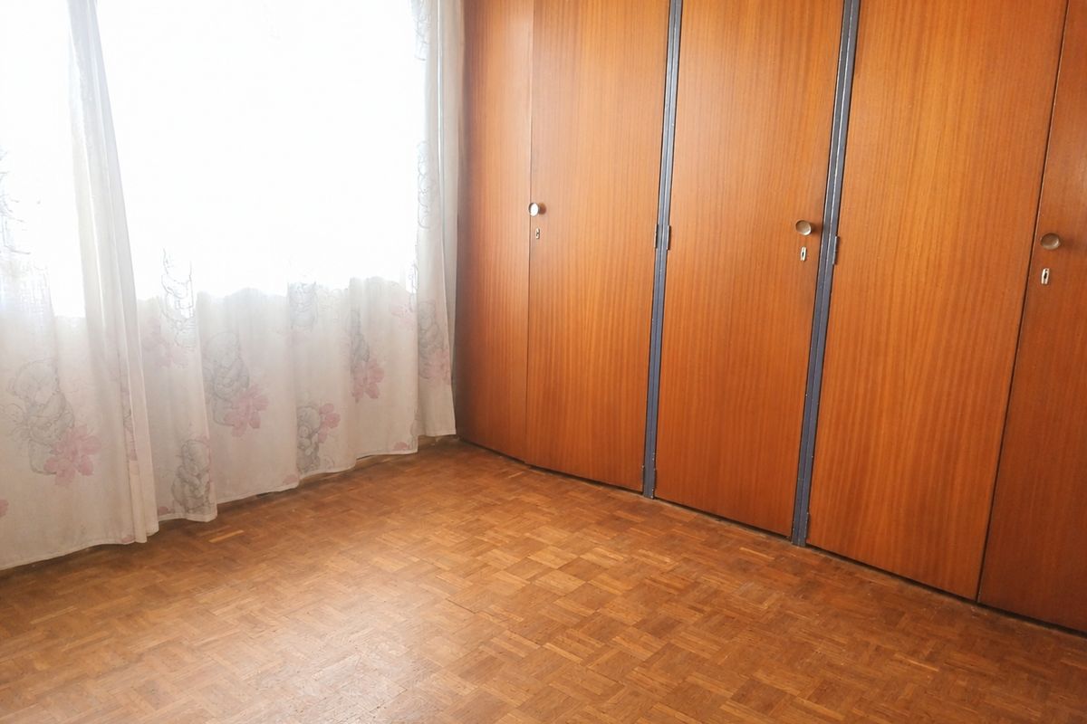A bedroom featuring classic parquet flooring and extensive built-in wooden cupboards, offering a functional space ready for modernization.