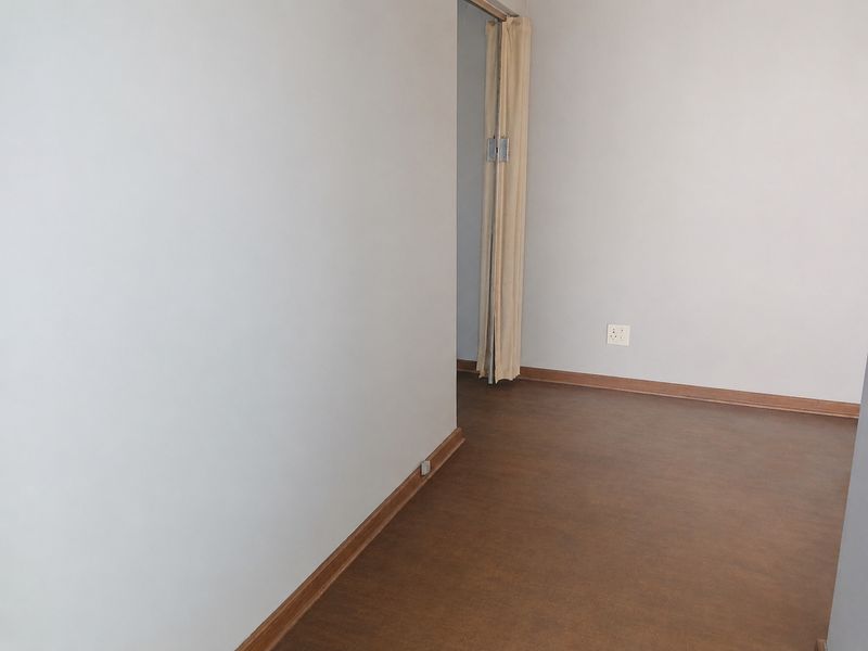 An empty hallway featuring neutral walls, dark flooring, and a folding door leading to an adjacent space.