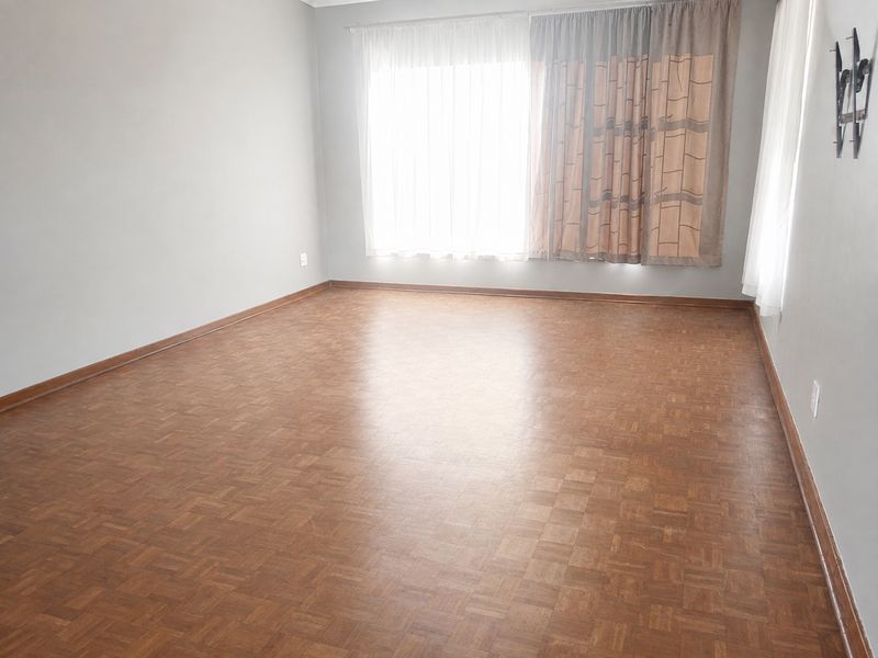 A spacious, empty living room featuring classic parquet flooring and neutral wall finishes, ready for personalization.