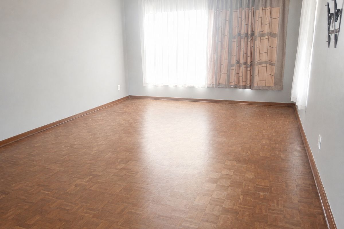 A spacious, empty living room featuring classic parquet flooring and neutral wall finishes, ready for personalization.