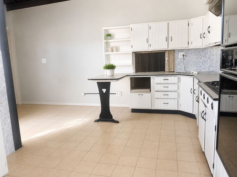 A functional kitchen featuring white cabinetry, tiled backsplash, built-in oven, and gas hob, with neutral tiled flooring throughout.