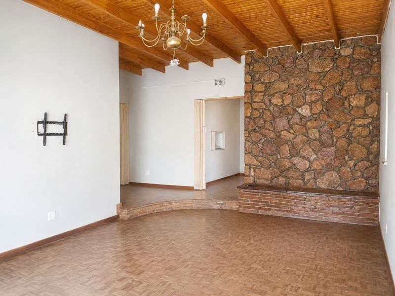Spacious living area featuring a rustic stone feature wall, brick hearth, exposed timber beam ceiling, and classic parquet flooring.