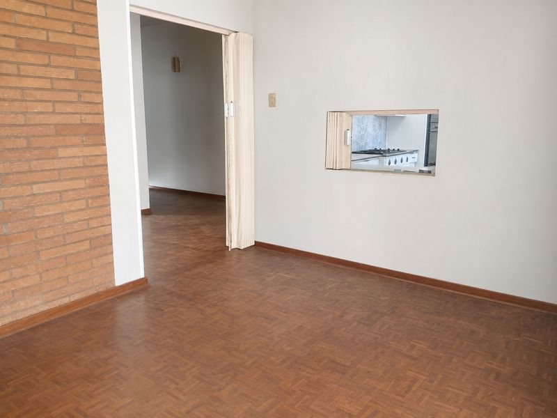 An empty living area featuring parquet flooring, an exposed brick wall, and a convenient serving hatch connecting to the kitchen space.