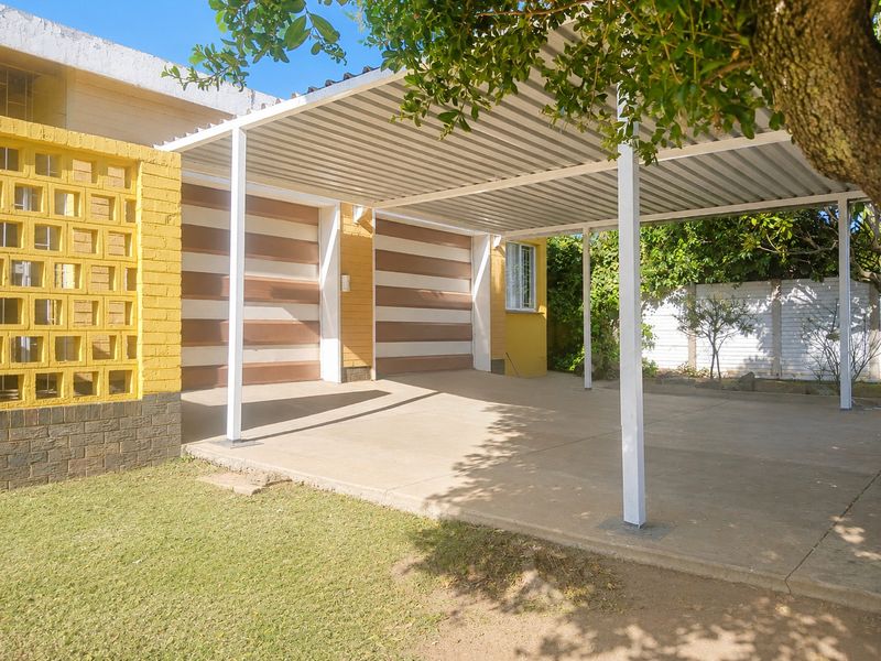 A double garage with an attached corrugated metal carport, featuring a decorative breeze block wall and a concrete driveway.