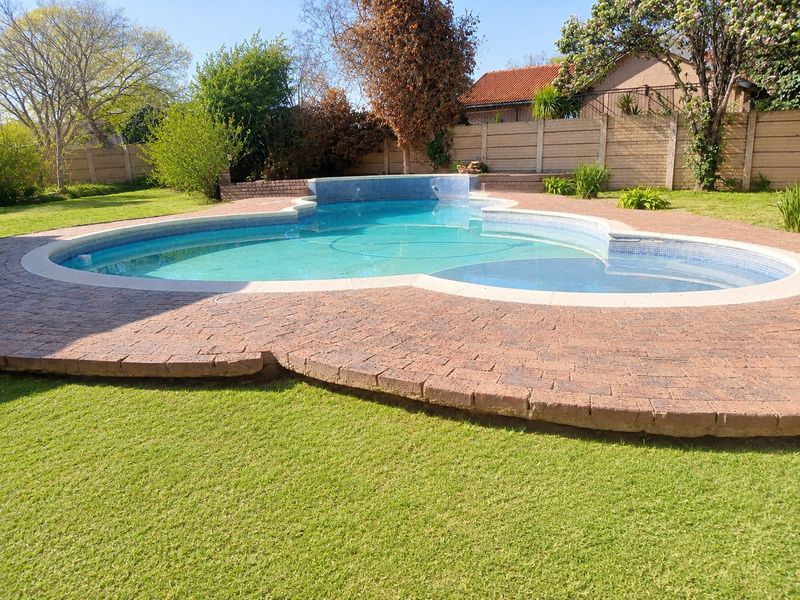 A backyard swimming pool featuring a curved design, surrounded by brick paving and a well-maintained lawn with a perimeter boundary wall.
