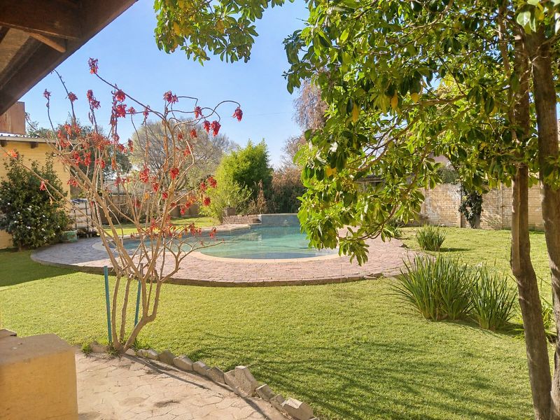 A private backyard featuring a swimming pool with a paved surround, set within a landscaped garden area with mature trees and boundary walls.
