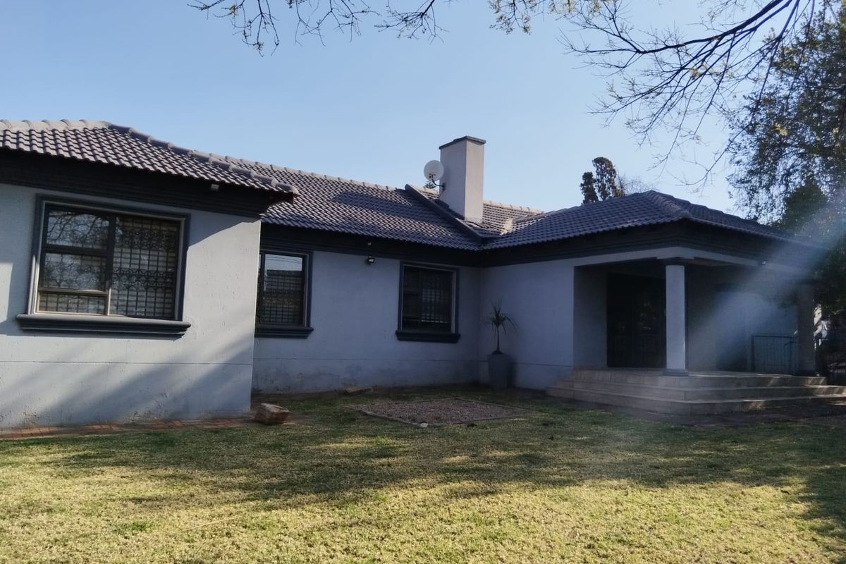 Rear view of the house featuring a tiled roof, chimney, and a covered patio area with concrete steps leading to the garden.