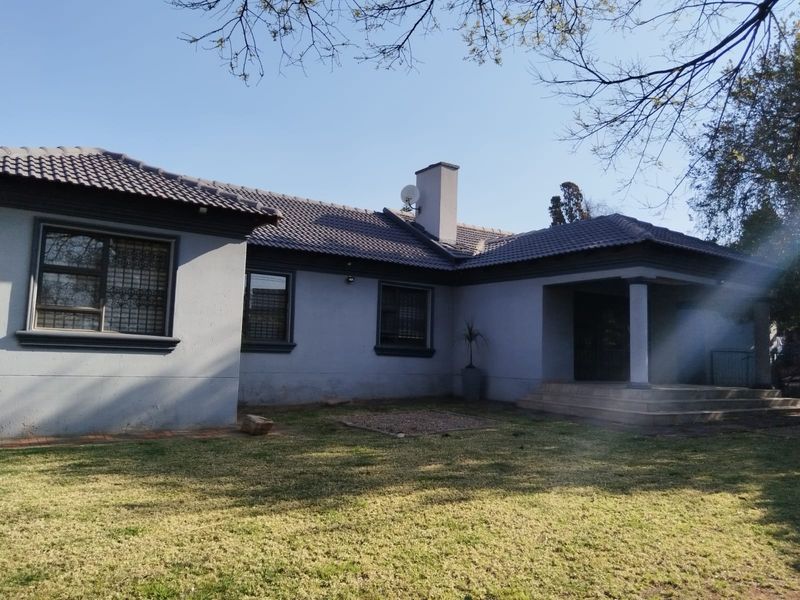 Rear view of the house featuring a tiled roof, chimney, and a covered patio area with concrete steps leading to the garden.