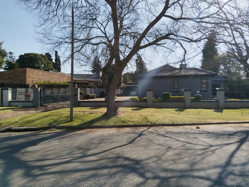Street view of the property showing the front perimeter wall, gated entrance, paved driveway, and main house structure with a tiled roof.