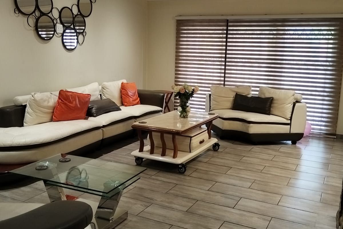 Spacious living room featuring wood-look floor tiles, a coffered ceiling with recessed lighting, and large windows fitted with modern venetian blinds.