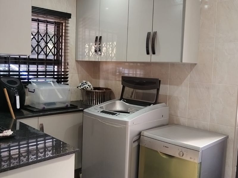 A functional laundry area featuring modern built-in cabinetry, granite countertops, tiled walls, and tiled flooring, providing efficient space for appliances and storage.