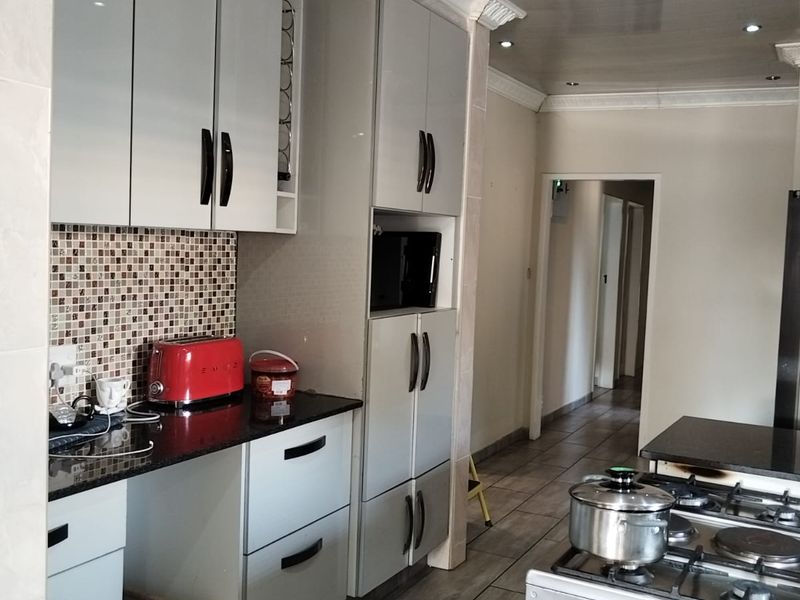 Modern kitchen featuring glossy cabinetry, granite countertops, mosaic tile backsplash, and a gas hob, with recessed lighting and crown molding details.