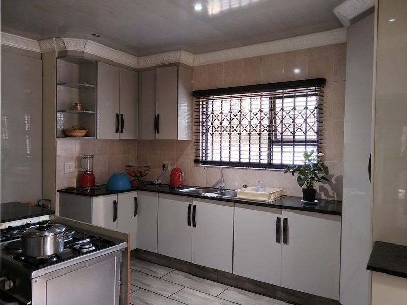A well-maintained kitchen featuring modern built-in cabinetry, granite countertops, a stainless steel gas hob, and a tiled backsplash with a secure window.