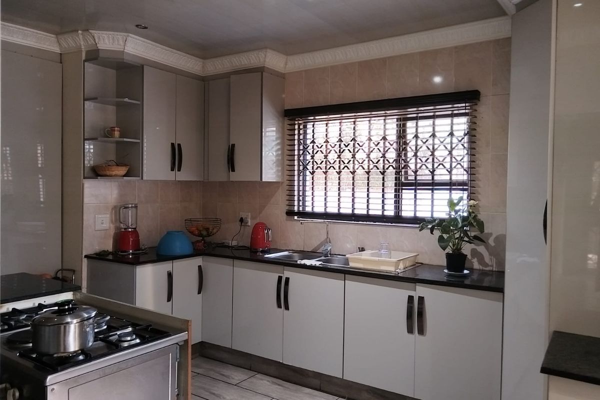 A well-maintained kitchen featuring modern built-in cabinetry, granite countertops, a stainless steel gas hob, and a tiled backsplash with a secure window.