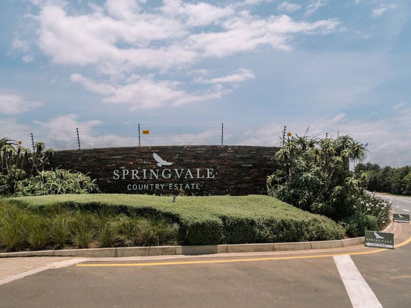 The entrance to Springvale Country Estate featuring a stone-clad signage wall, manicured landscaping, and secure electric fencing.