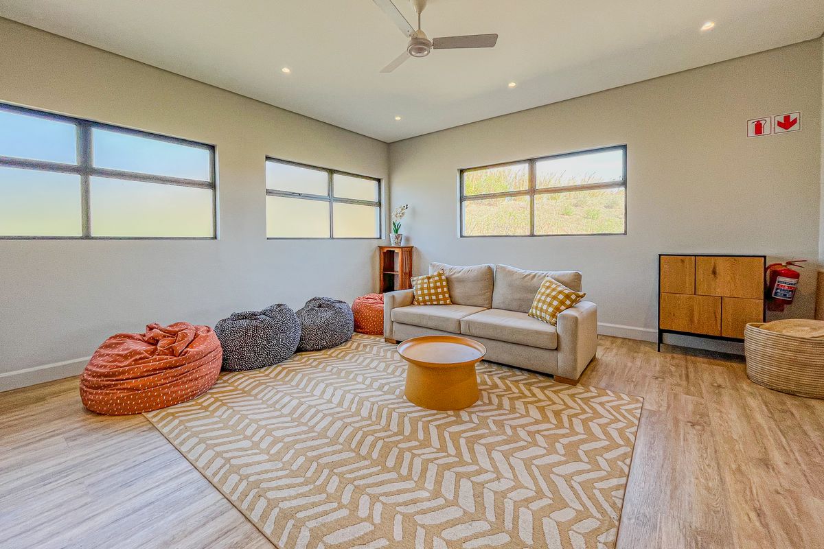 A bright and modern living room featuring laminate flooring, recessed lighting, a ceiling fan, and large windows providing ample natural light.