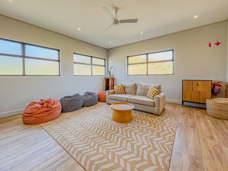 A bright and modern living room featuring laminate flooring, recessed lighting, a ceiling fan, and large windows providing ample natural light.