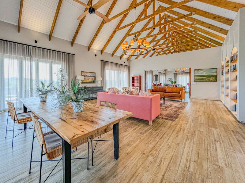Spacious open-plan living and dining area featuring high vaulted ceilings with exposed timber trusses, built-in shelving, and abundant natural light.