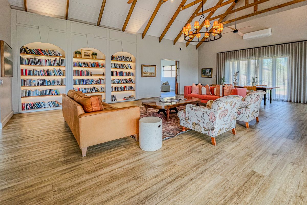 Spacious living room featuring a high vaulted ceiling with exposed timber rafters, built-in arched bookshelves, and modern wood-look flooring.