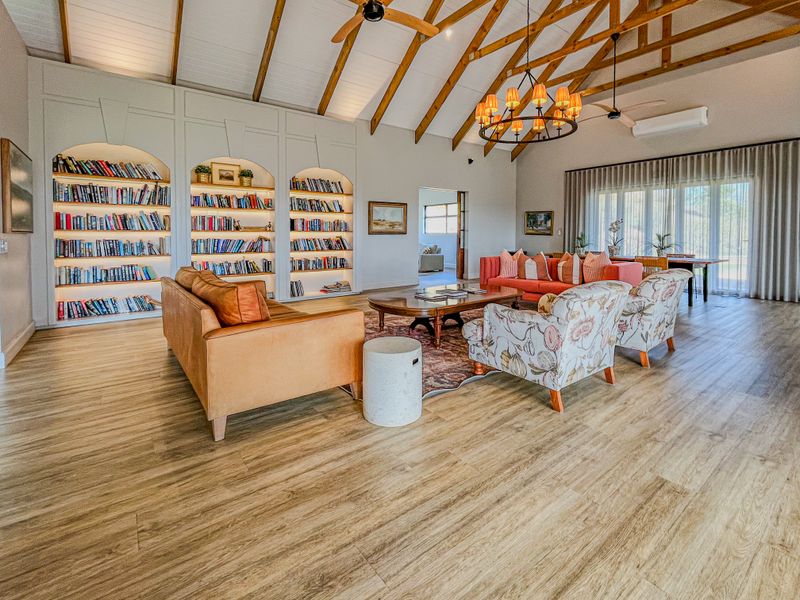 Spacious living room featuring a high vaulted ceiling with exposed timber rafters, built-in arched bookshelves, and modern wood-look flooring.