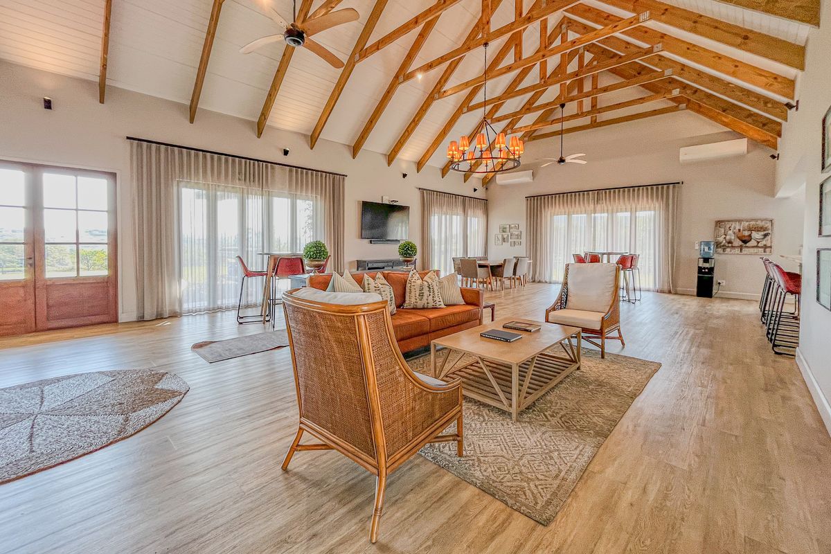 Spacious open-plan living area featuring high vaulted ceilings with exposed timber trusses, timber flooring, and large glass doors providing ample natural light.