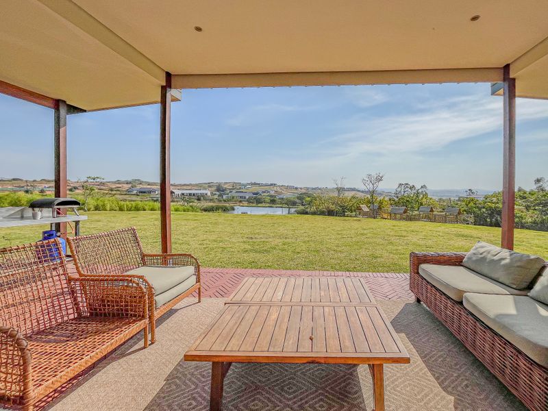 A spacious covered patio featuring brick paving and timber supports, offering expansive views over the landscaped lawn and surrounding estate landscape.