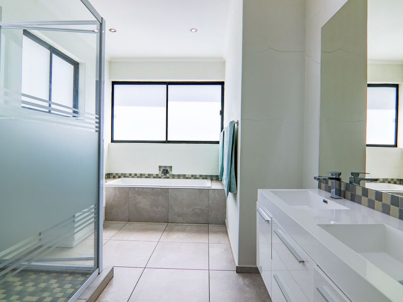 Modern bathroom featuring a double vanity, built-in bathtub, and a glass-enclosed shower with neutral tile finishes.