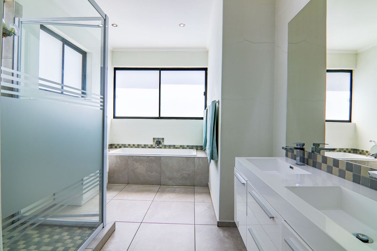 Modern bathroom featuring a double vanity, built-in bathtub, and a glass-enclosed shower with neutral tile finishes.