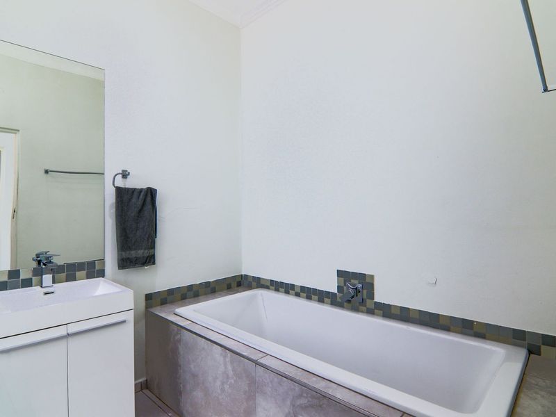 A functional bathroom featuring a built-in vanity with basin, a bathtub with tiled surround, and a wall-mounted mirror.