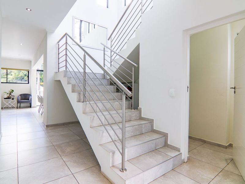 Bright and modern entrance hallway featuring a tiled staircase with stainless steel balustrades and clean, neutral finishes.