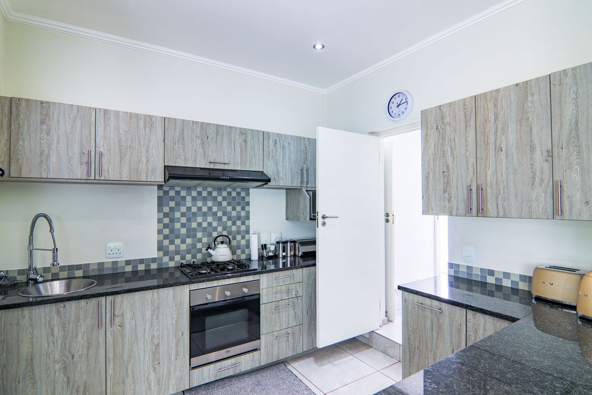 Modern kitchen featuring wood-grain cabinetry, granite countertops, a gas hob, electric oven, and a stylish mosaic tile backsplash.